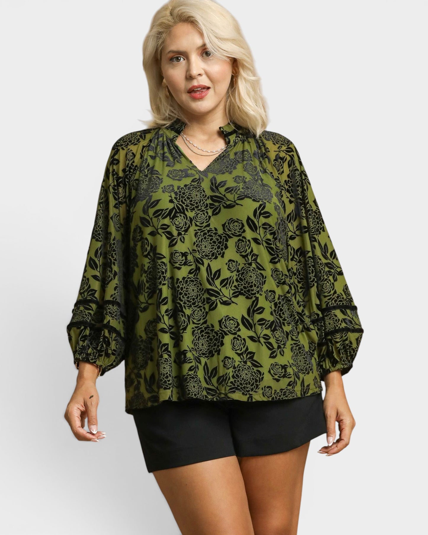 Woman wearing a green floral blouse and black shorts on a white background