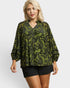 Woman wearing a green floral blouse and black shorts on a white background