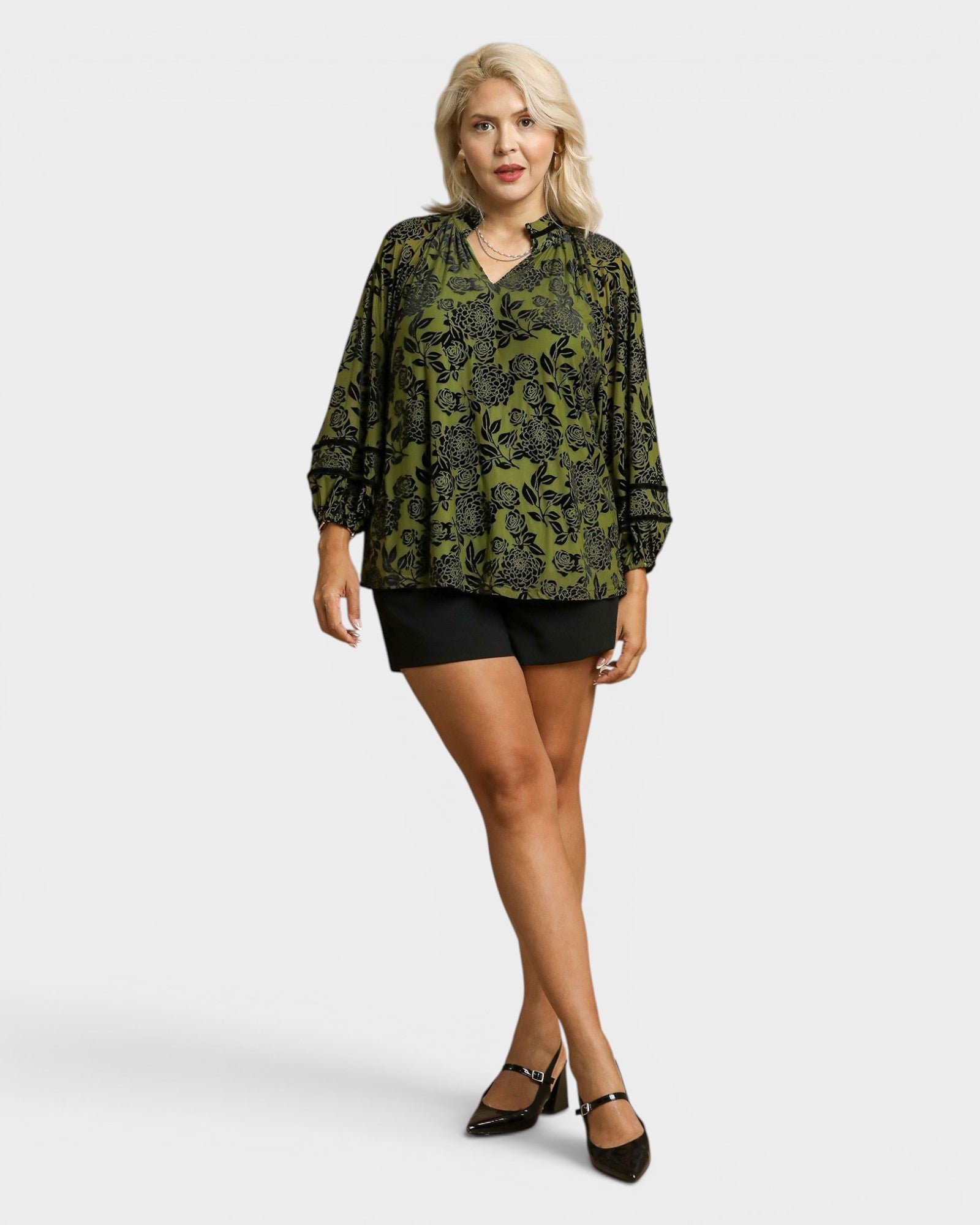 Woman wearing a green patterned blouse and black shorts on a white background