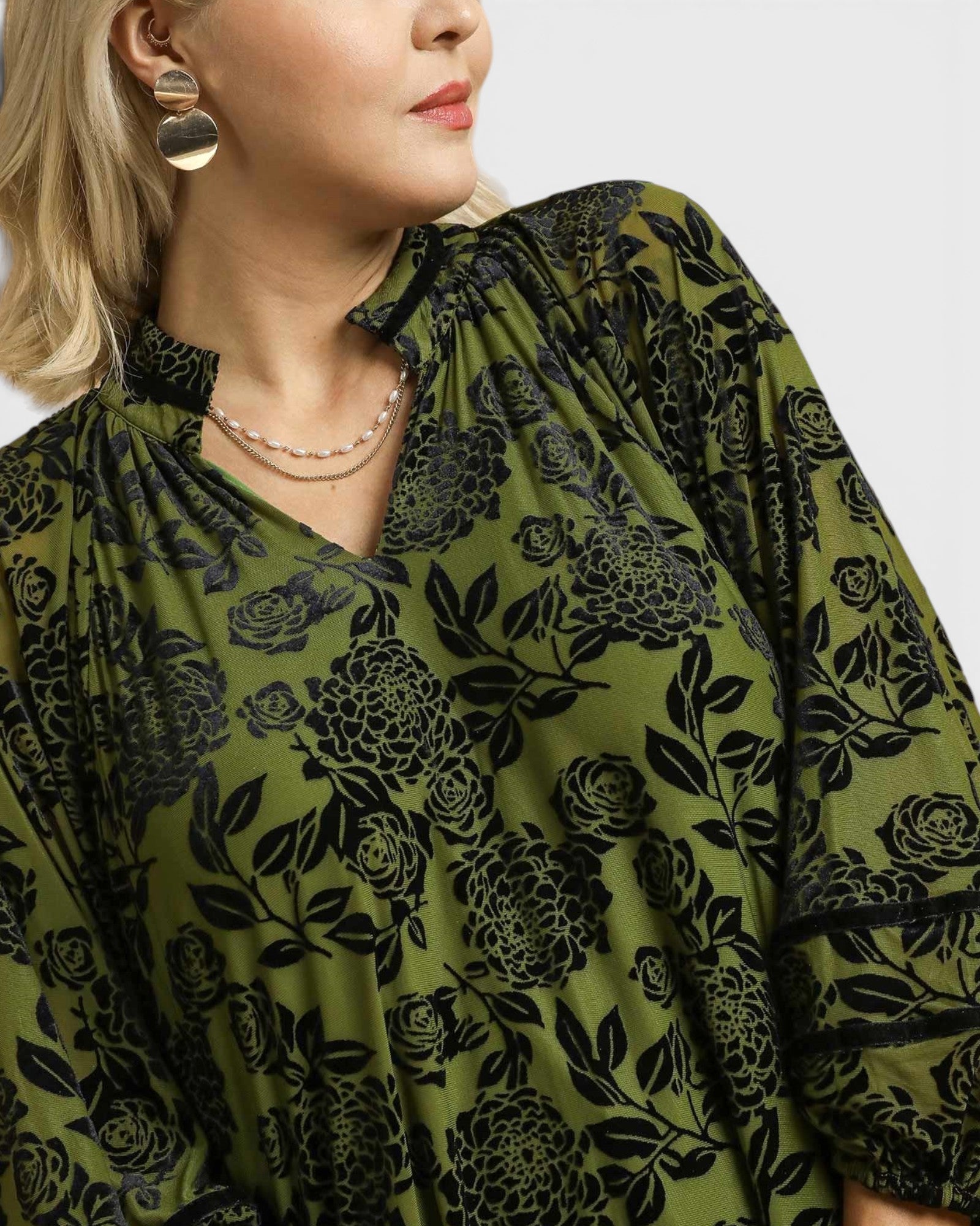 Woman wearing a green floral patterned dress with a plain background