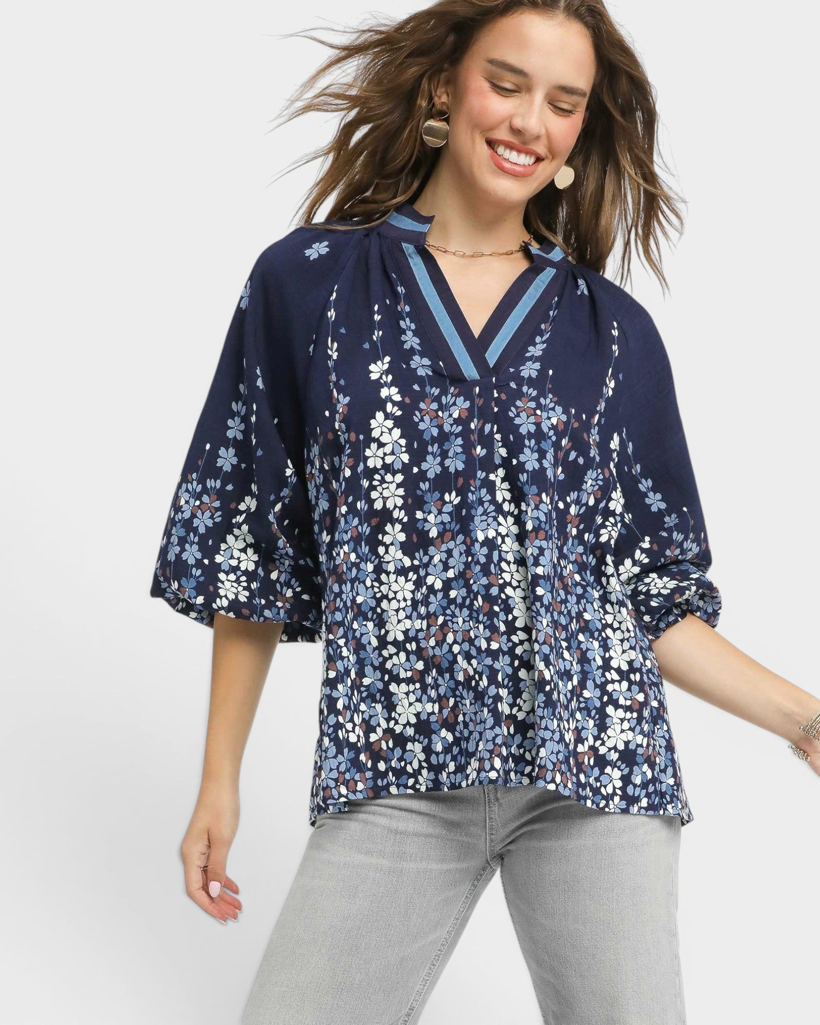 Woman wearing a navy floral blouse with gray pants on a light gray background