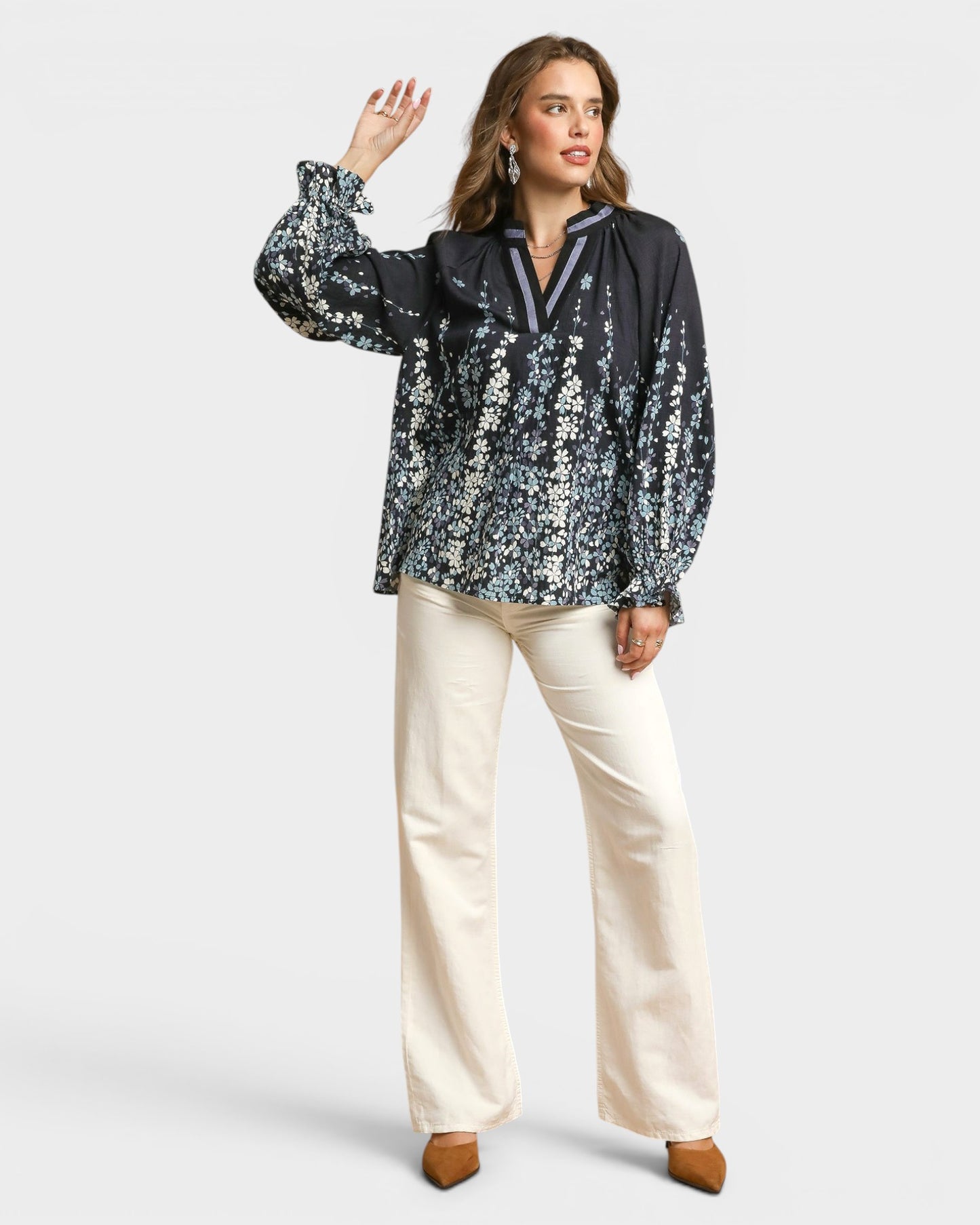 Woman wearing a black floral blouse and white pants on a white background