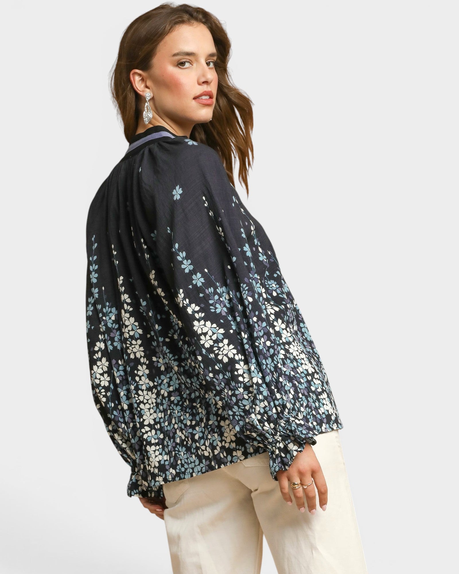 Woman wearing a black floral blouse with beige pants on a light gray background