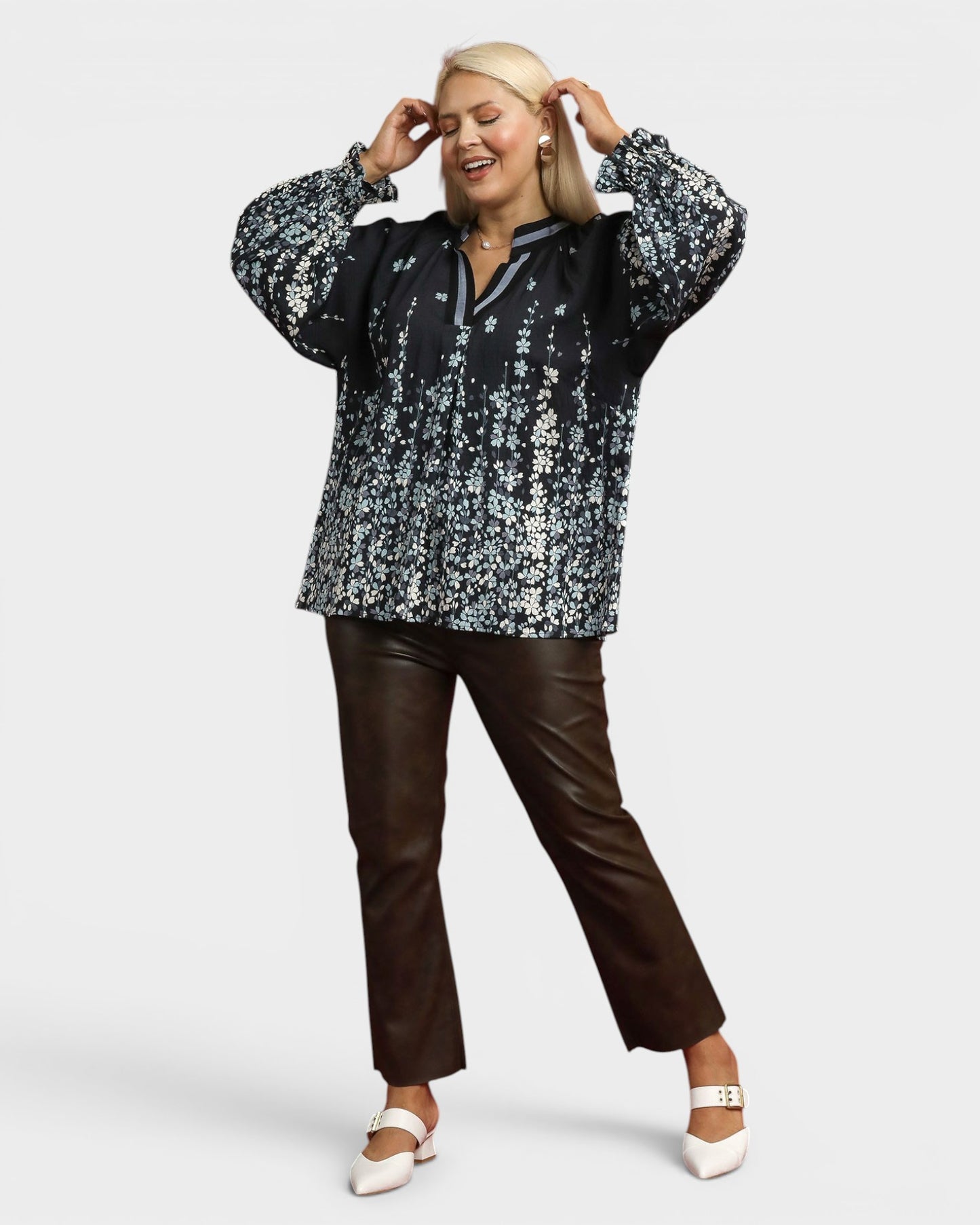 Woman wearing a black floral blouse and brown pants on a white background