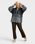 Woman wearing a black floral blouse and brown pants on a white background
