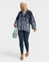 Woman wearing a navy floral blouse and jeans holding a light blue handbag on a white background