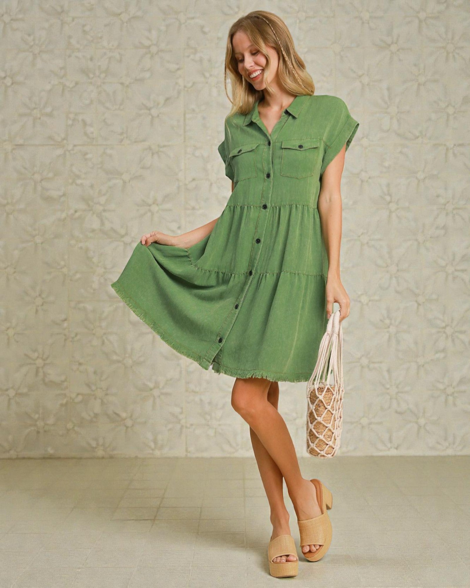 Woman wearing a green dress holding a bag against a neutral background