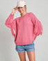 Woman wearing a pink fringe sweater and denim shorts on a plain background