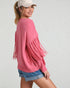 Woman wearing a pink fringed sweater and denim shorts on a light gray background