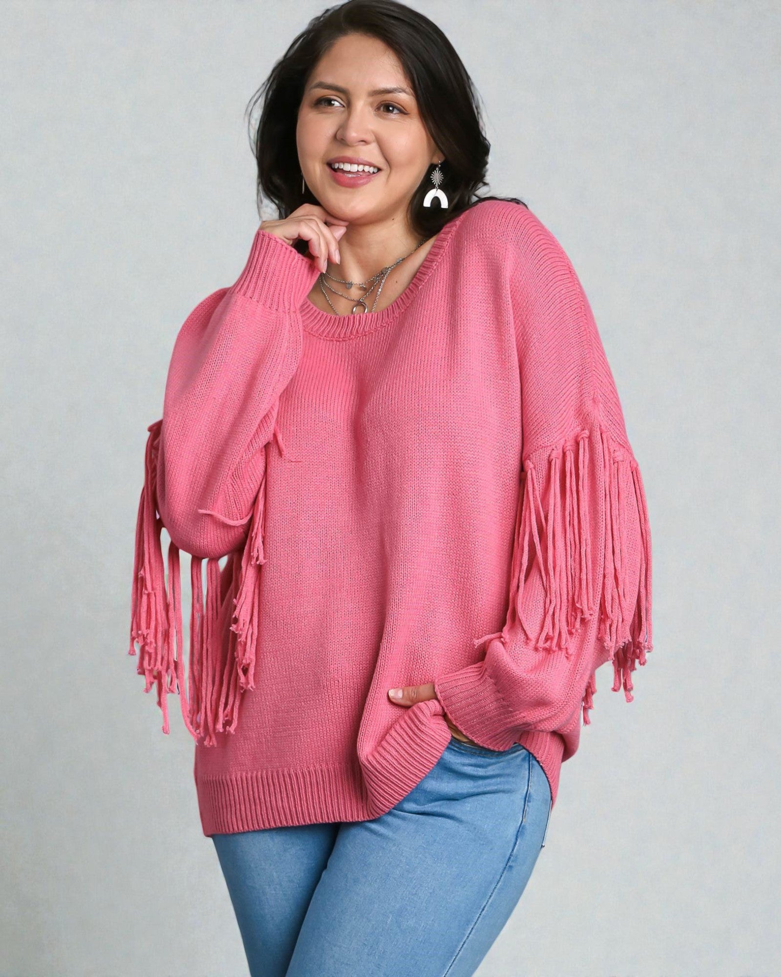 Woman wearing a pink sweater with fringe details on a gray background