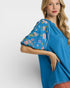 Woman wearing a blue dress with floral embroidery on a white background