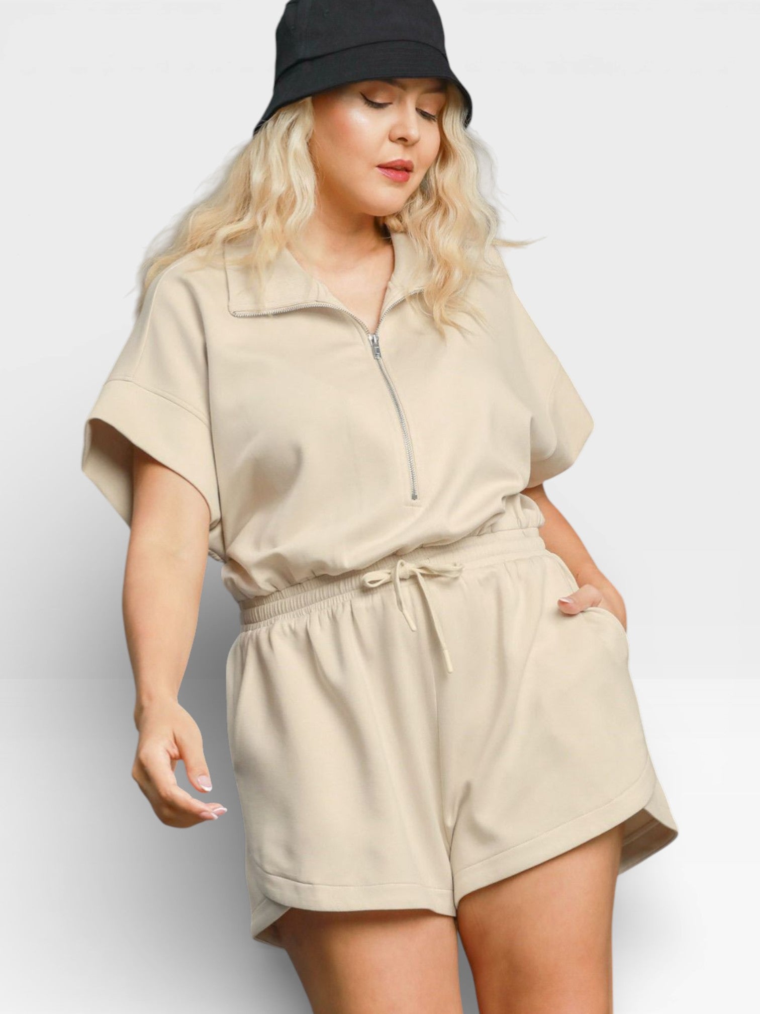 Woman wearing a beige romper and black hat on a white background