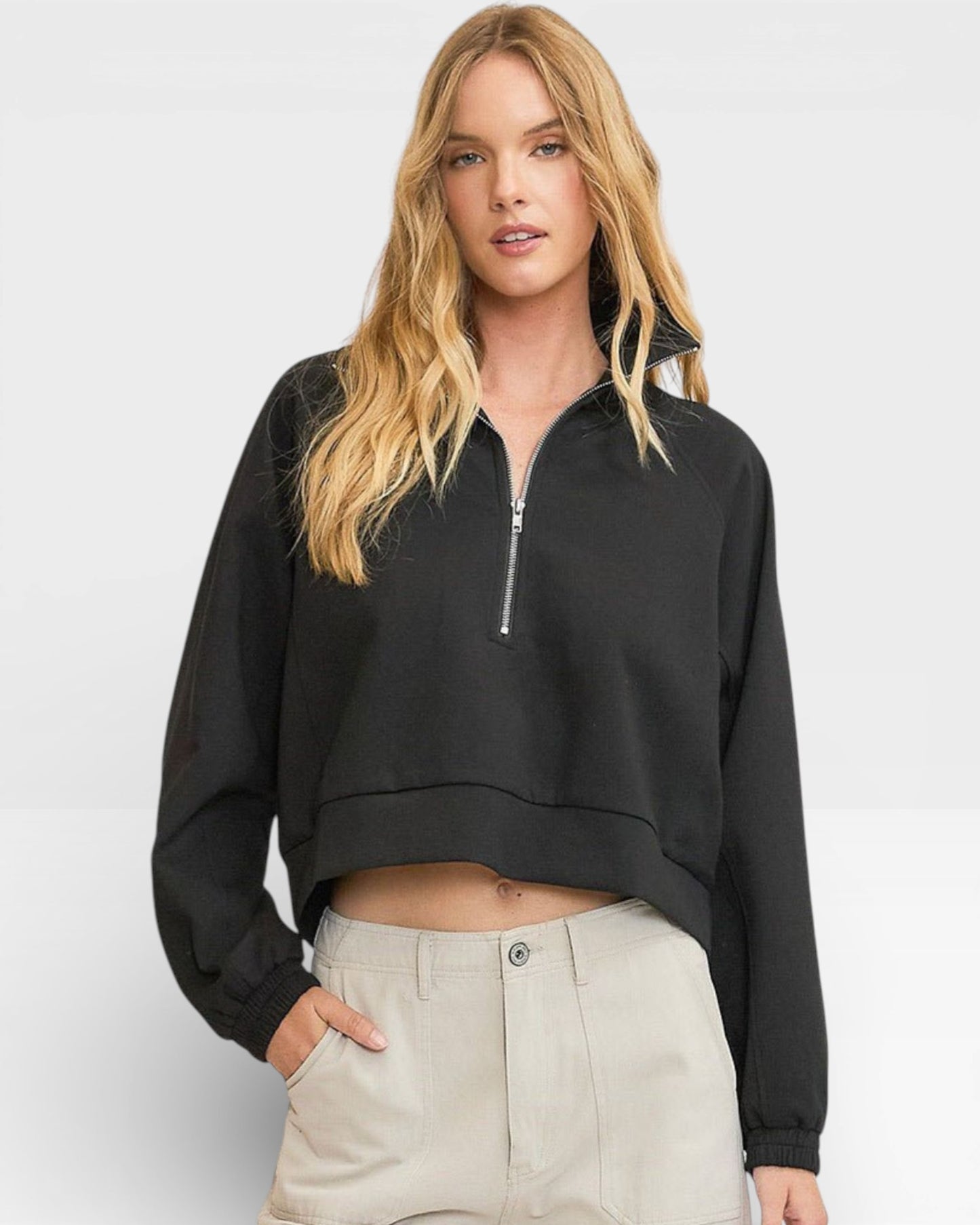 Woman wearing a black cropped hoodie with a zipper on a plain background
