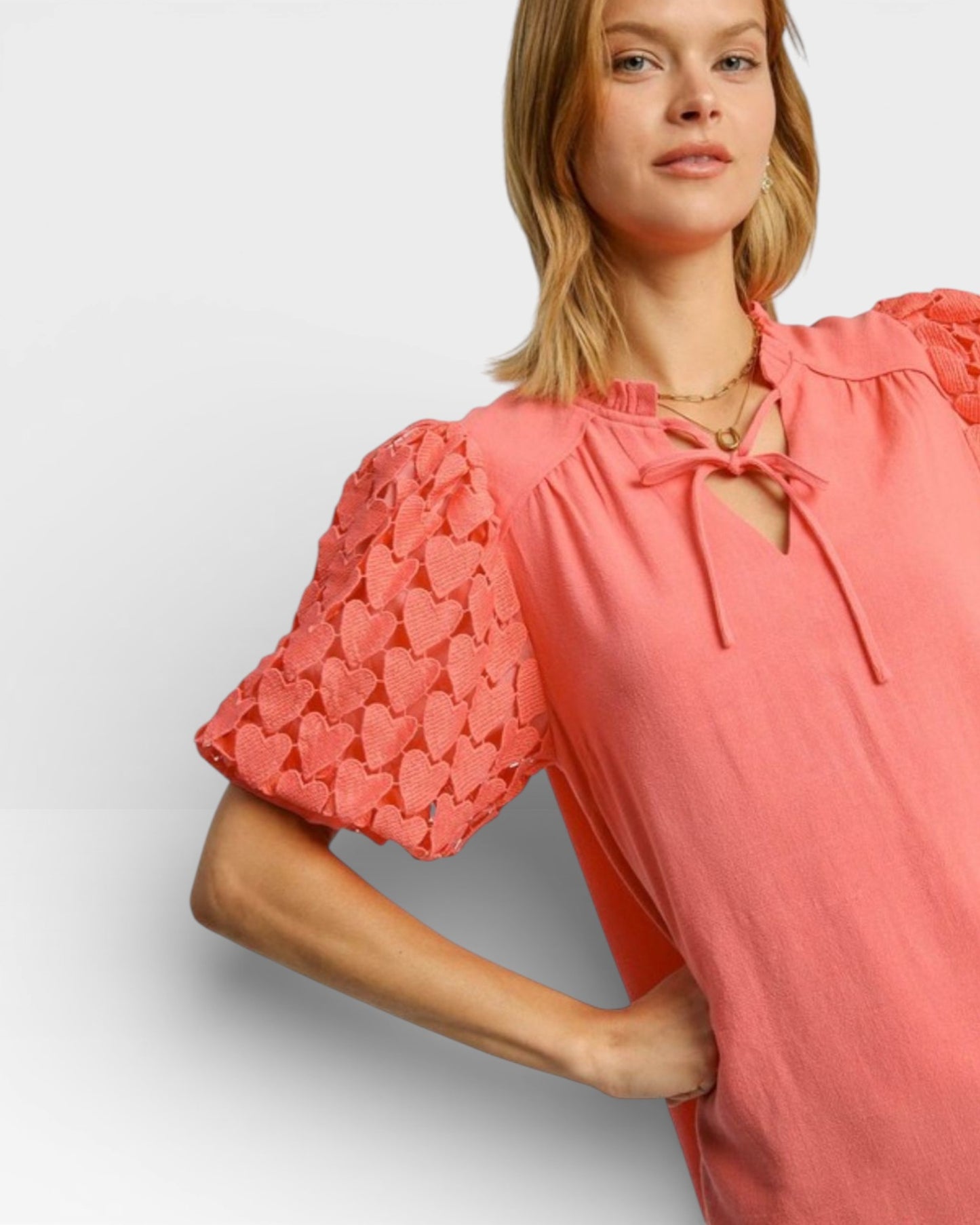Woman wearing a coral pink blouse with heart patterns on sleeves against a light gray background