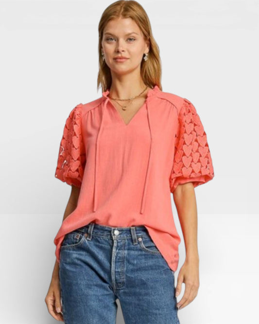 Woman wearing a coral blouse with ruffled sleeves and blue jeans on a white background