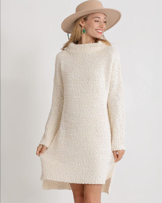 Woman wearing a cream-colored textured dress with a beige hat on a white background