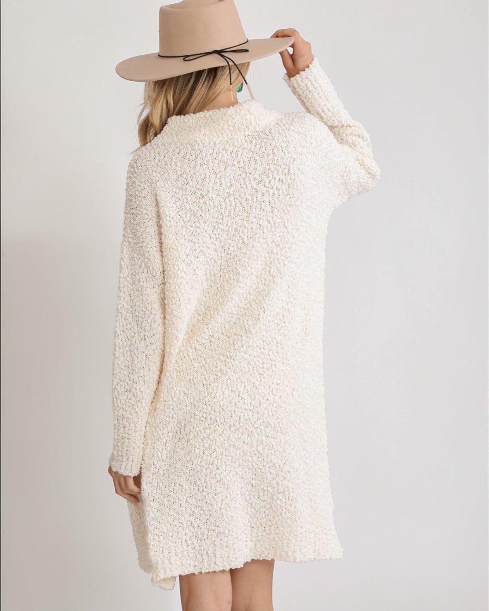 Person wearing a cream-colored sweater dress and beige hat on a plain background