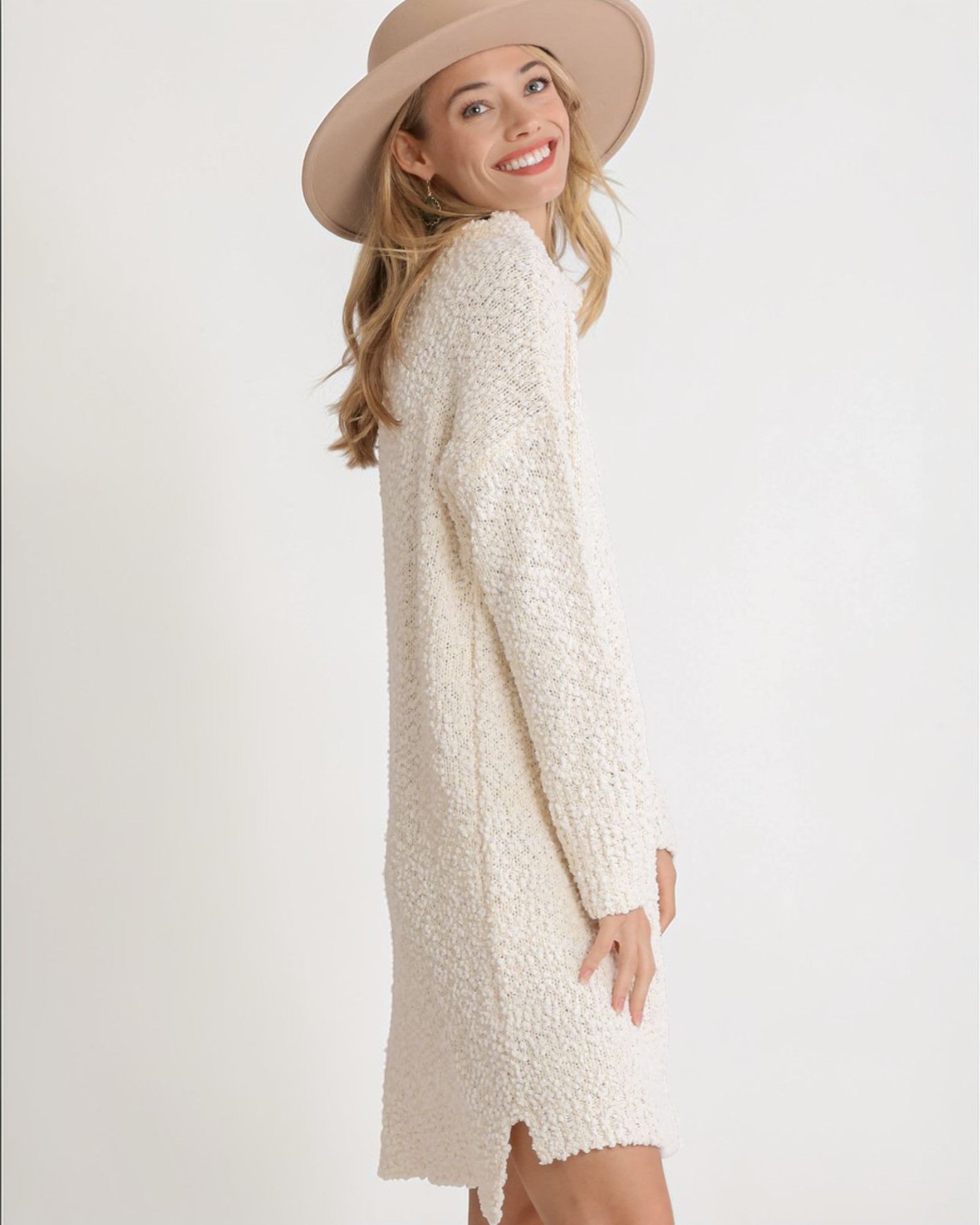 Woman wearing a cream-colored textured dress and beige hat on a white background