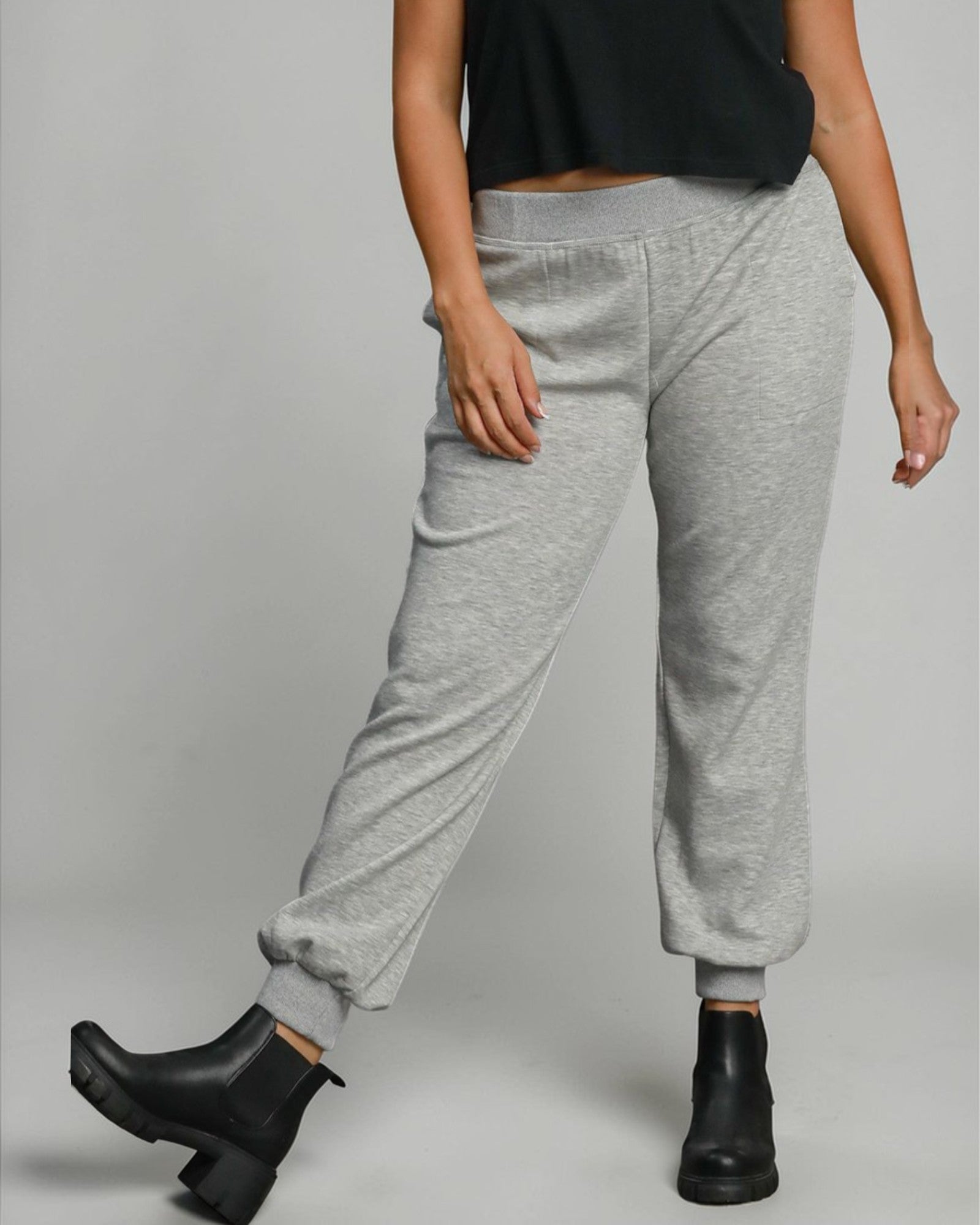 Person wearing gray sweatpants and black boots on a plain background