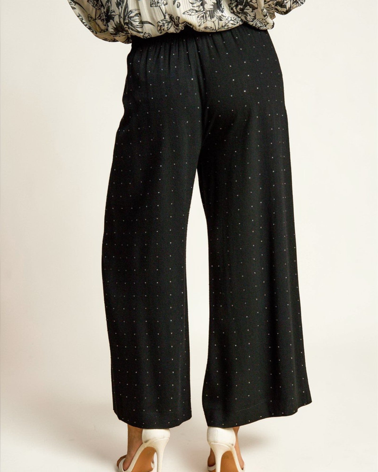 Black polka dot pants worn by a person on a plain background