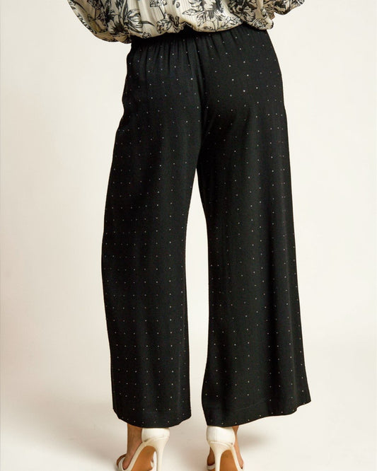 Black polka dot pants worn by a person on a plain background