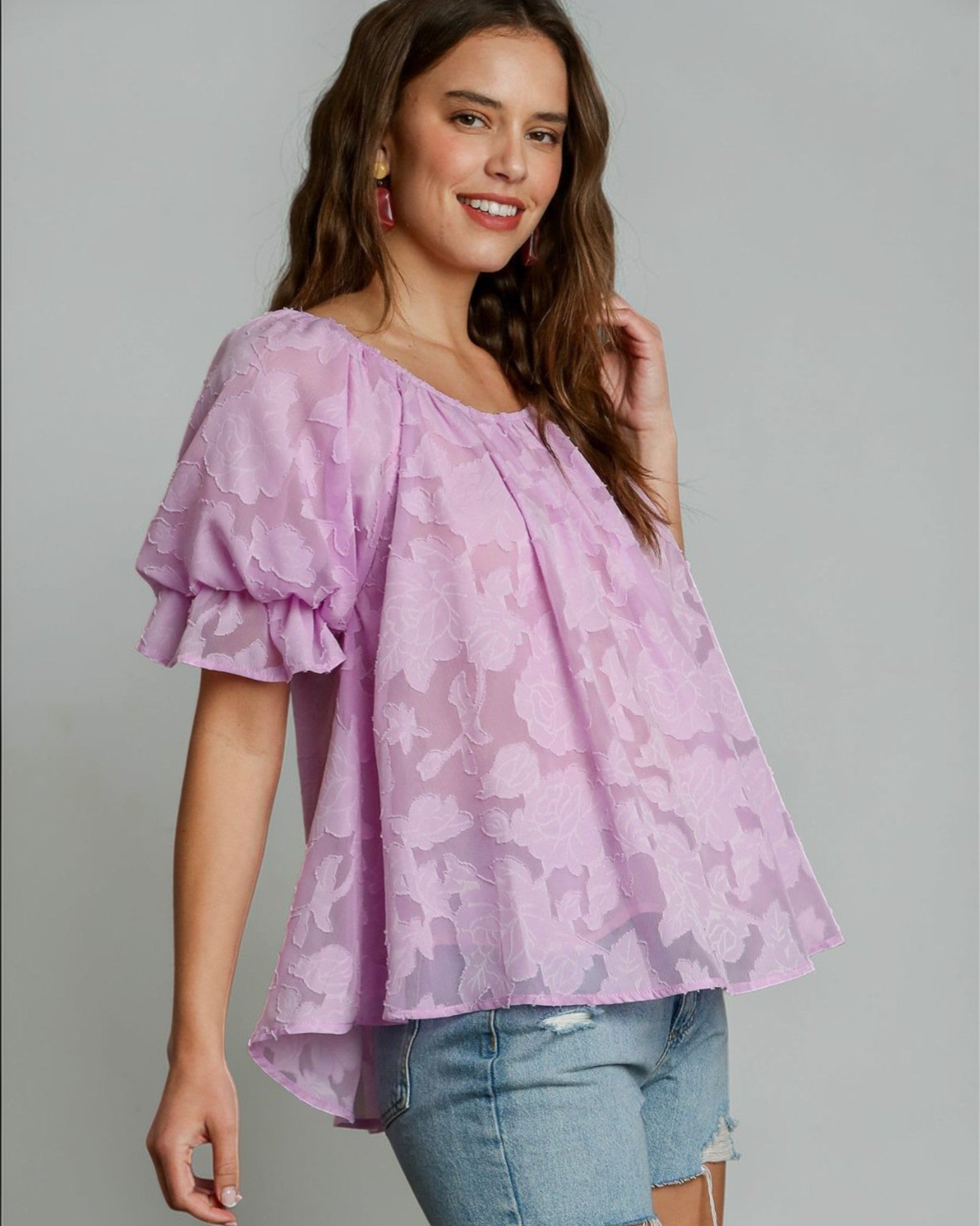 Woman wearing a pink floral blouse and denim shorts on a gray background
