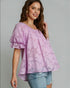 Woman wearing a pink floral blouse and denim shorts on a gray background