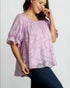 Woman wearing a light purple blouse with a subtle pattern on a plain background