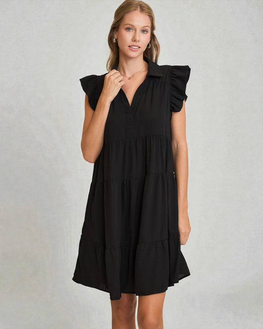 Woman wearing a black dress with ruffled sleeves against a plain background