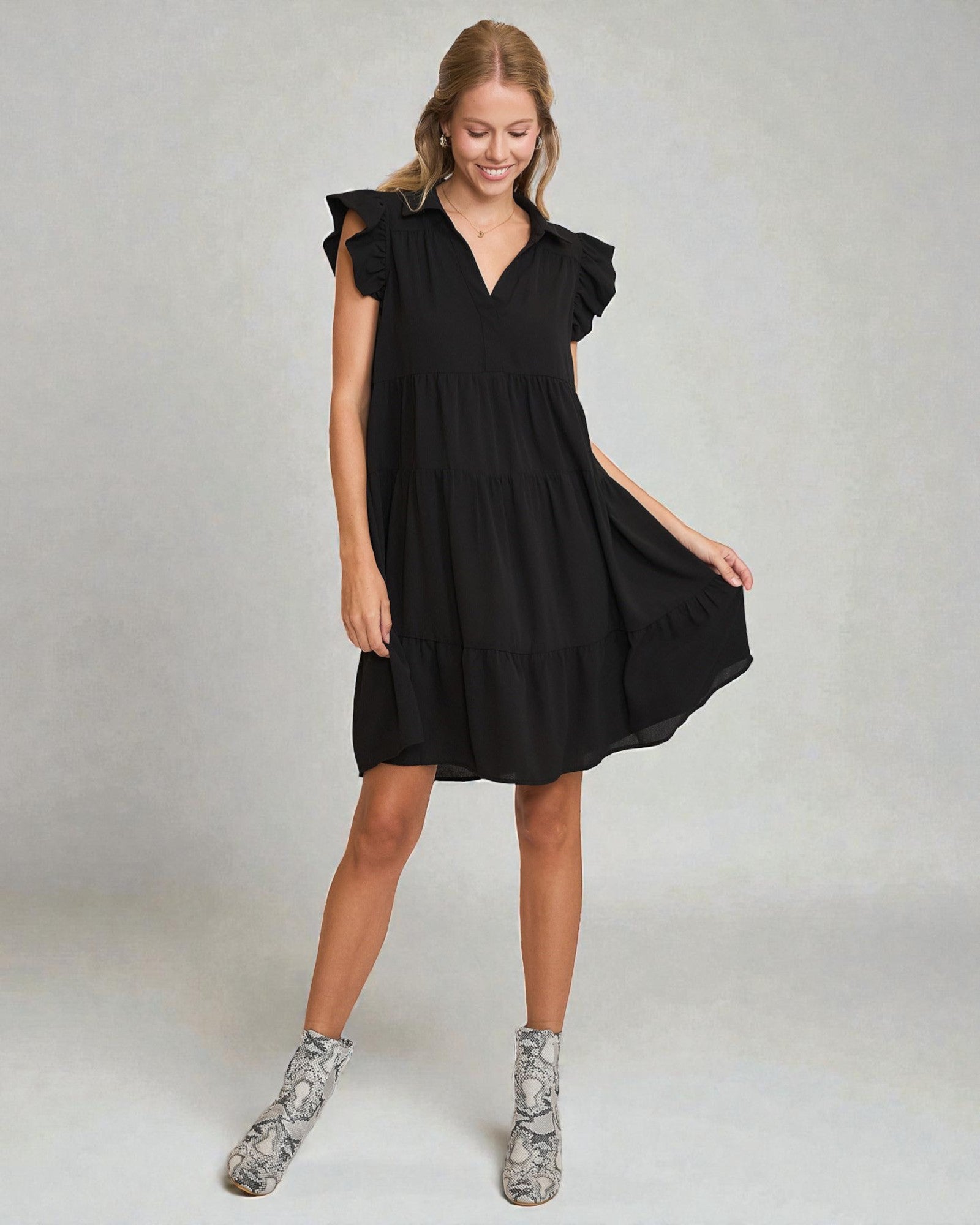 Woman wearing a black dress with ruffled sleeves on a plain background