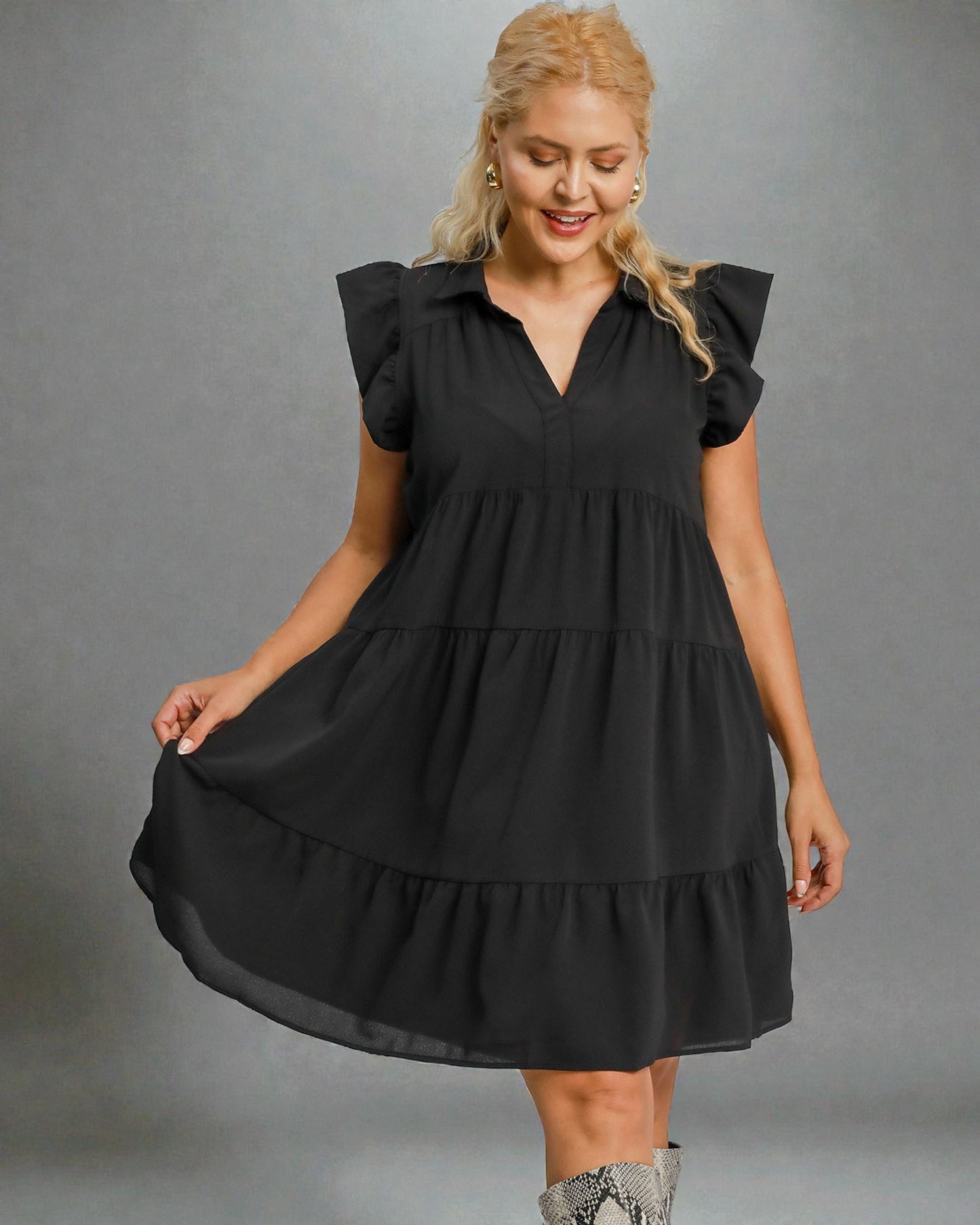 Woman wearing a black dress with ruffled sleeves against a gray background