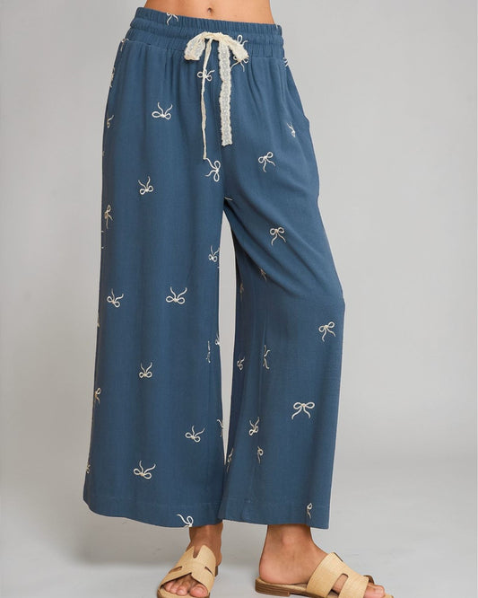 Blue pants with white bow pattern worn by a person on a gray background