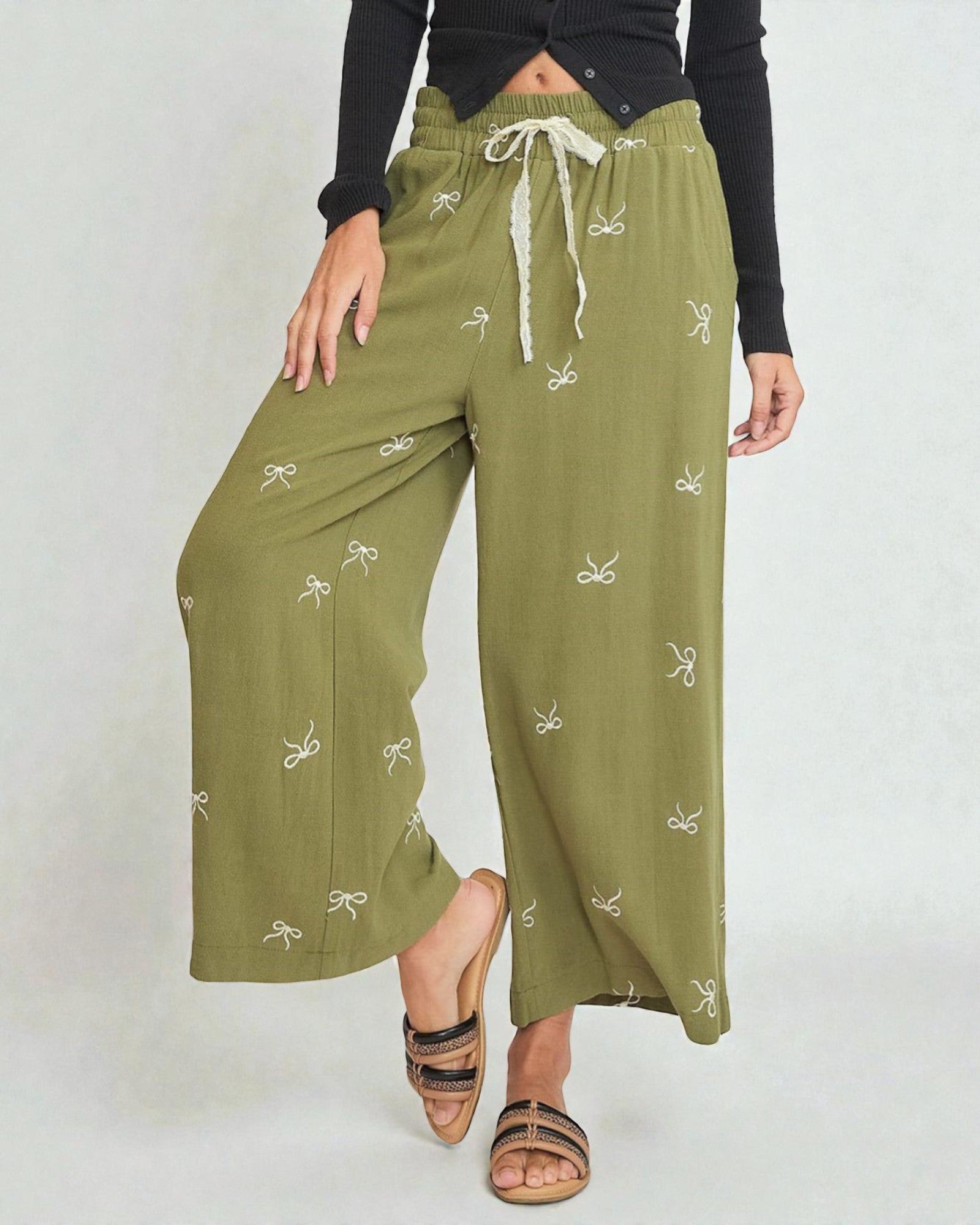 Person wearing olive green pants with a white pattern on a plain background