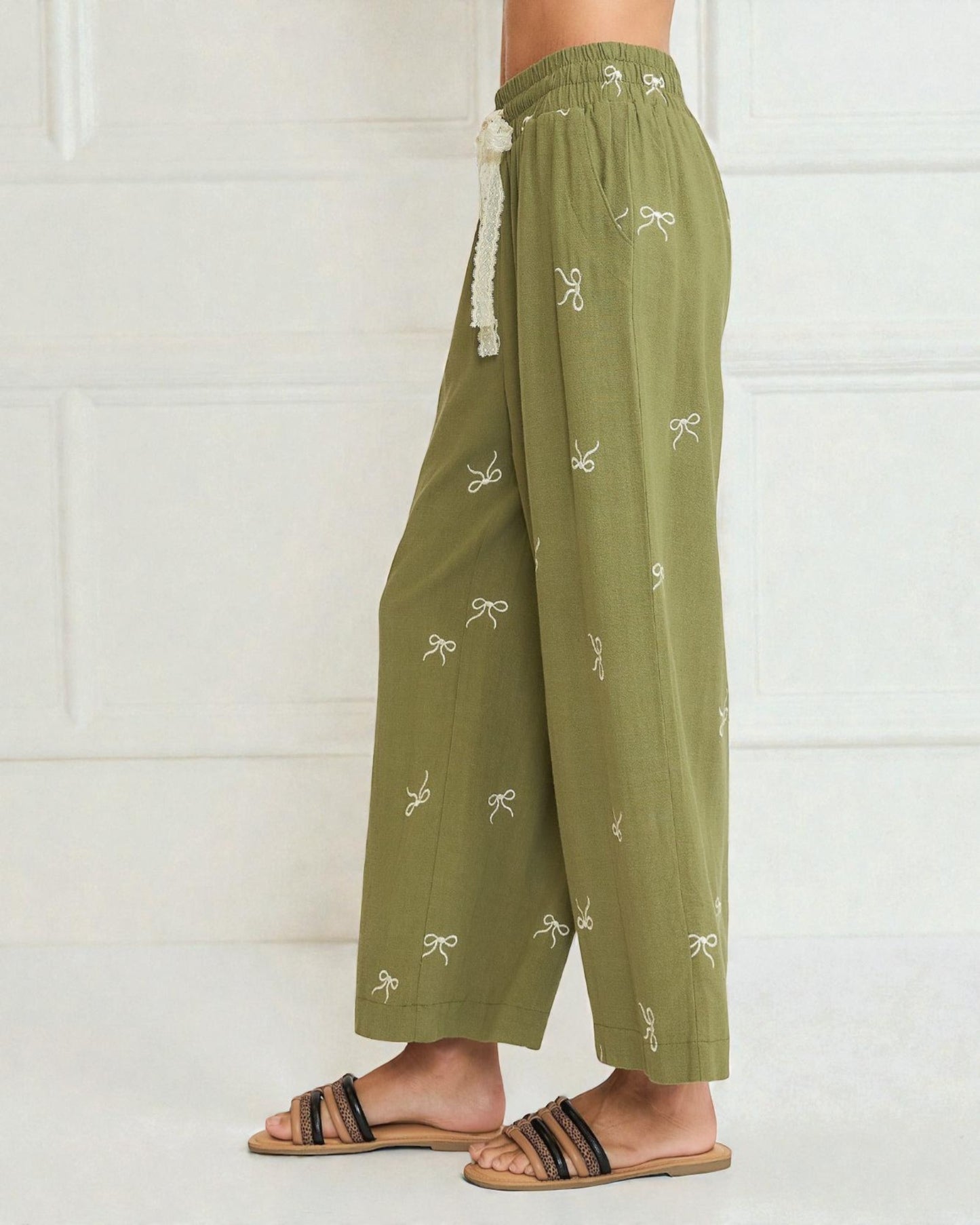 Green pants with white bow patterns worn by a person on a white background
