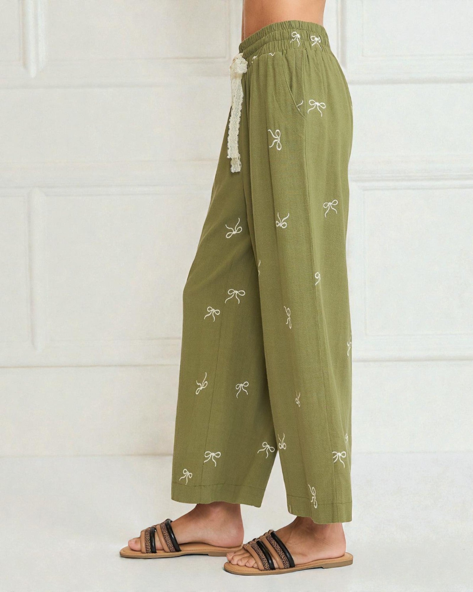 Green pants with white bow patterns worn by a person on a white background