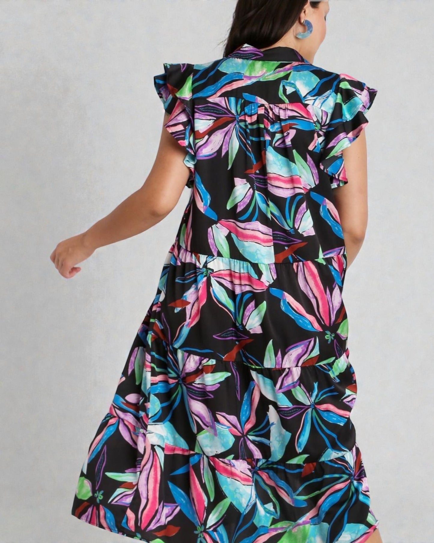 Woman wearing a colorful floral dress with ruffled sleeves on a plain background