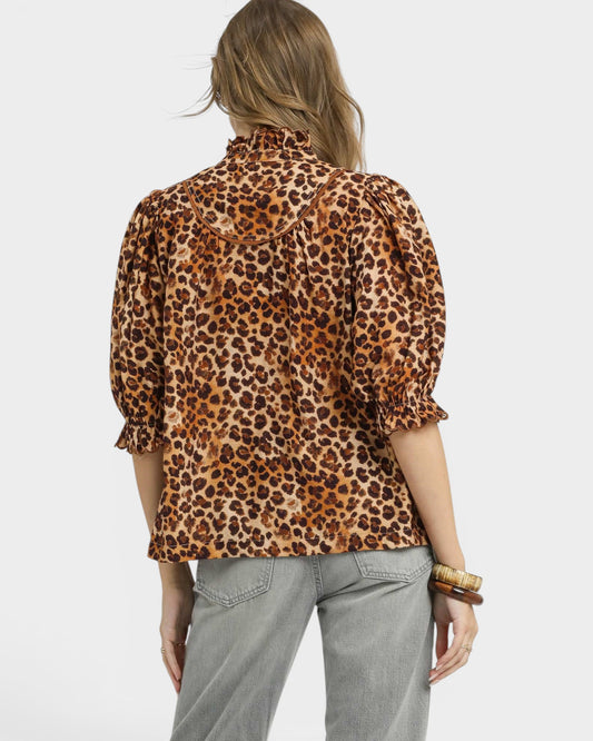 Person wearing a leopard print blouse and light gray pants on a white background