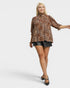 Woman wearing a leopard print blouse and black shorts on a white background