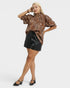 Woman wearing a leopard print blouse and black leather shorts on a white background