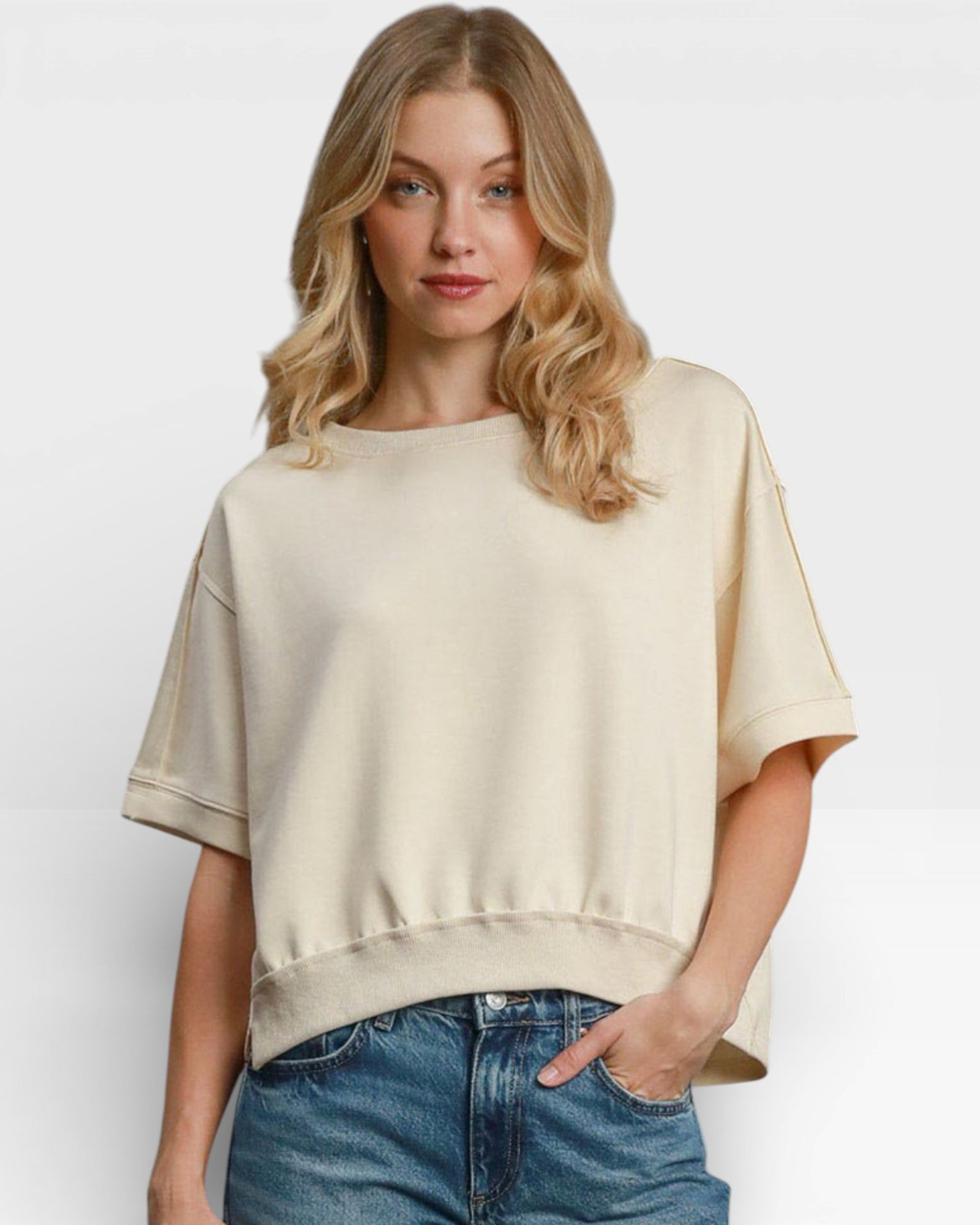 Woman wearing a beige oversized shirt and blue jeans on a white background