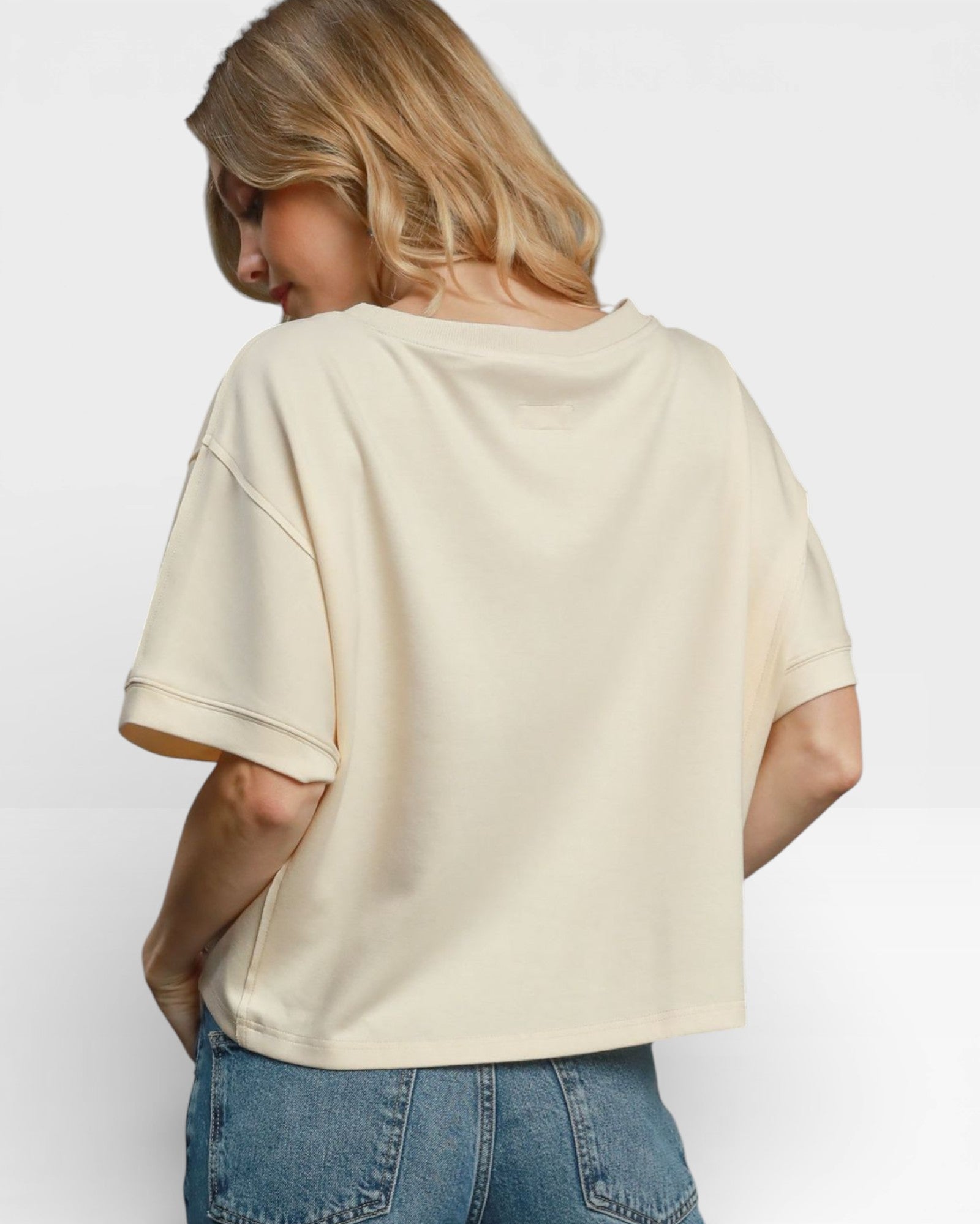 Person wearing a beige t-shirt and blue jeans on a white background