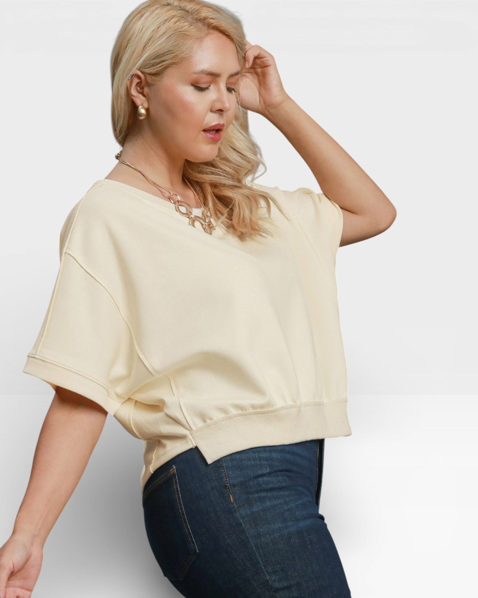 Woman wearing a beige top and dark jeans against a white background
