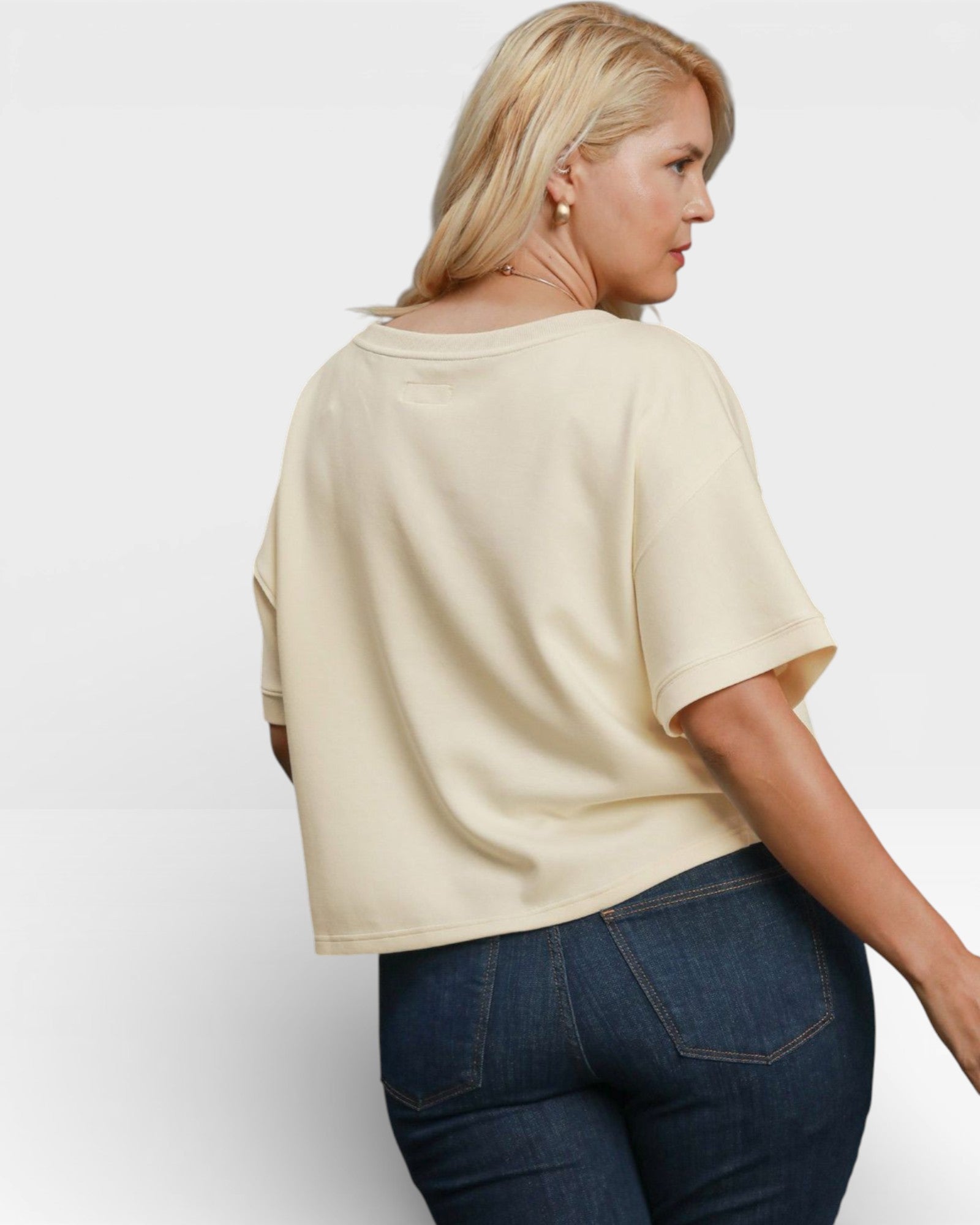 Woman wearing a beige oversized t-shirt and blue jeans on a white background