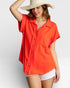Woman wearing an orange shirt and white shorts with a straw hat on a light gray background