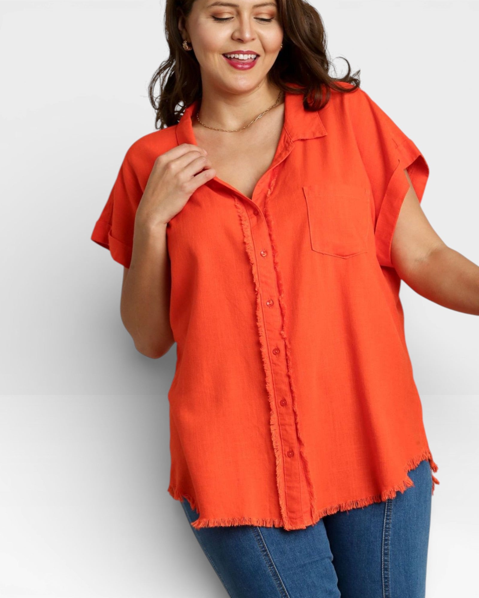 Woman wearing an orange button-up shirt and blue jeans on a white background