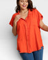 Woman wearing an orange button-up shirt and blue jeans on a white background