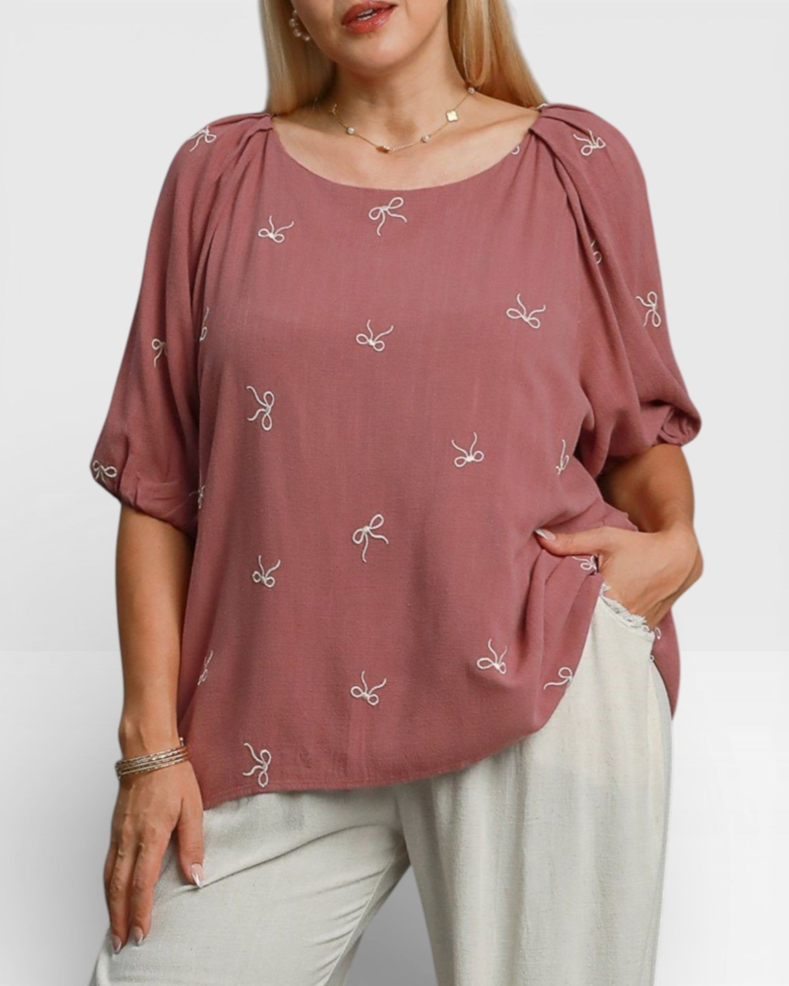 Woman wearing a mauve blouse with white patterns on a plain background