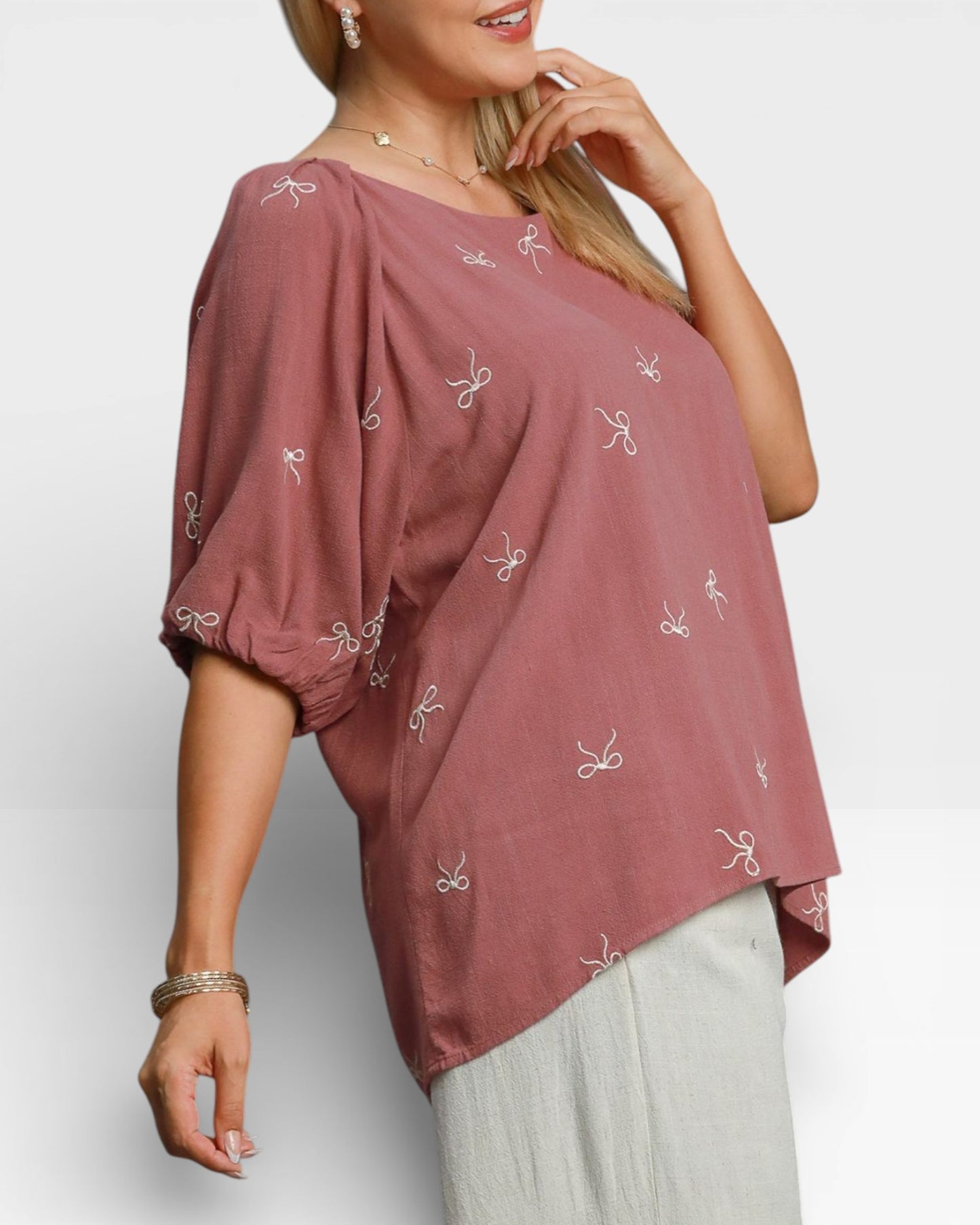 Woman wearing a mauve top with white patterns on a plain background