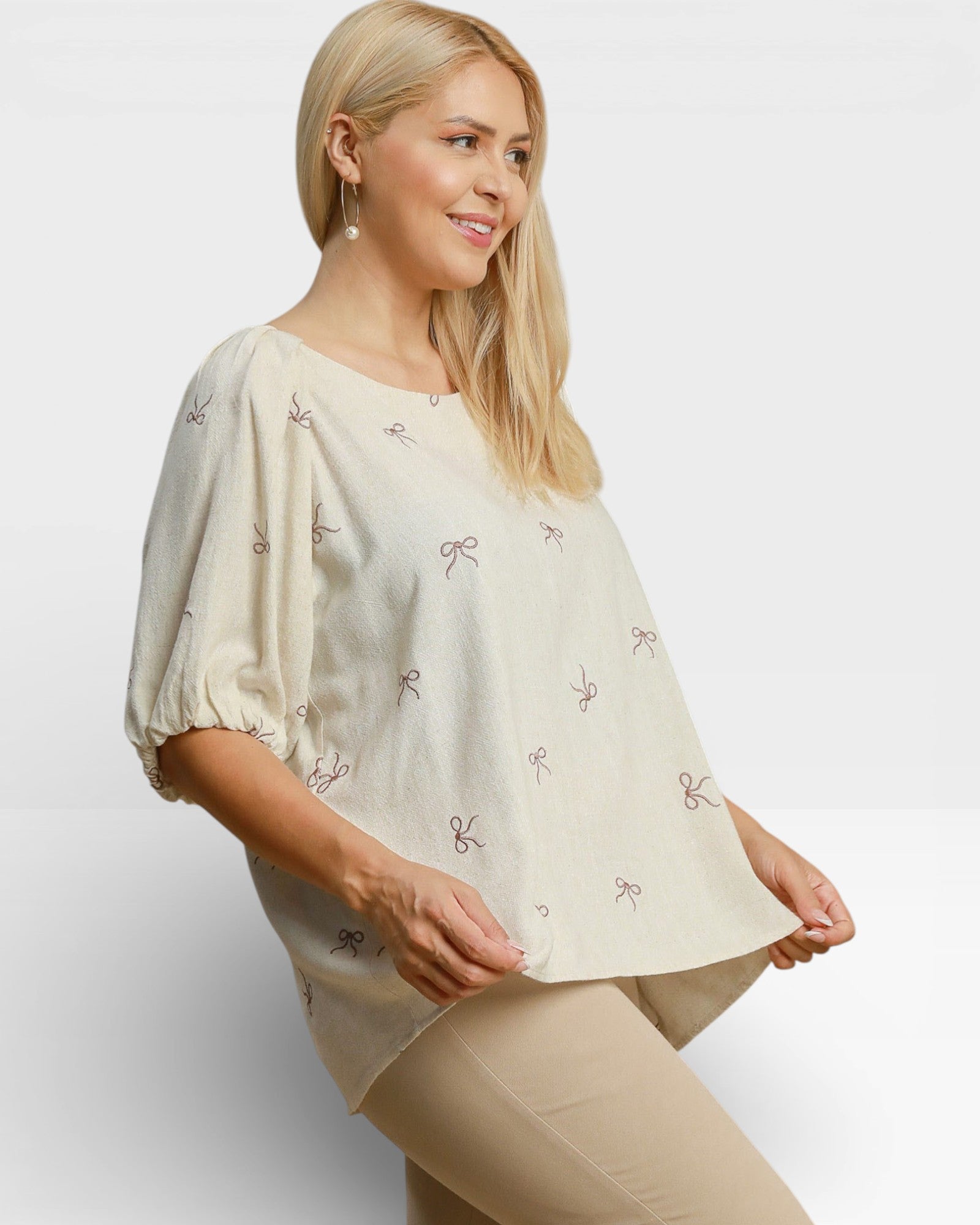 Woman wearing a beige blouse with bow patterns on a plain background