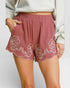 Pink shorts with floral embroidery worn by a person on a plain background